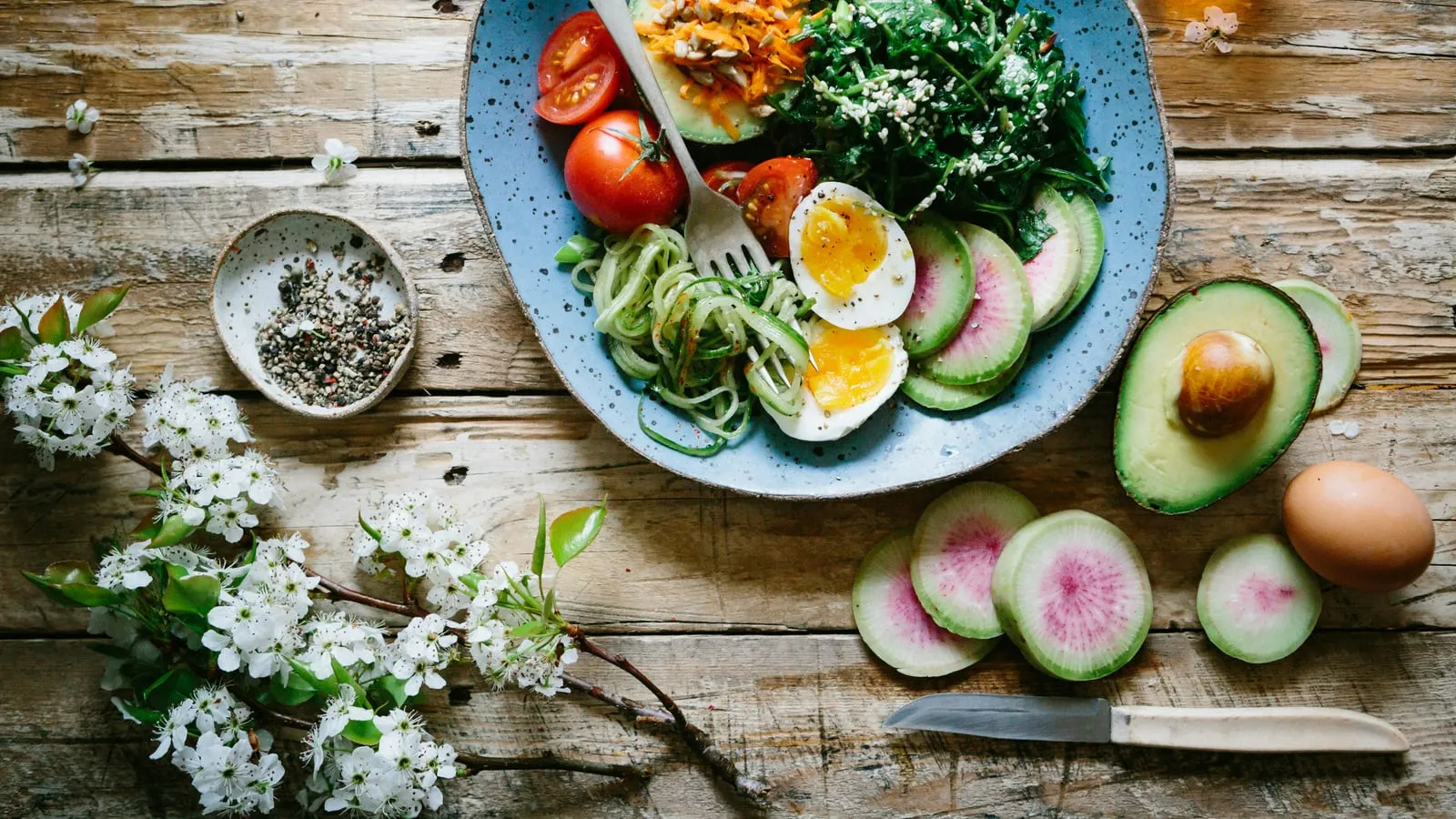 Vista aérea de mesa com variedade de vegetais frescos, grãos e temperos coloridos sob luz natural, em composição que celebra comida de verdade
