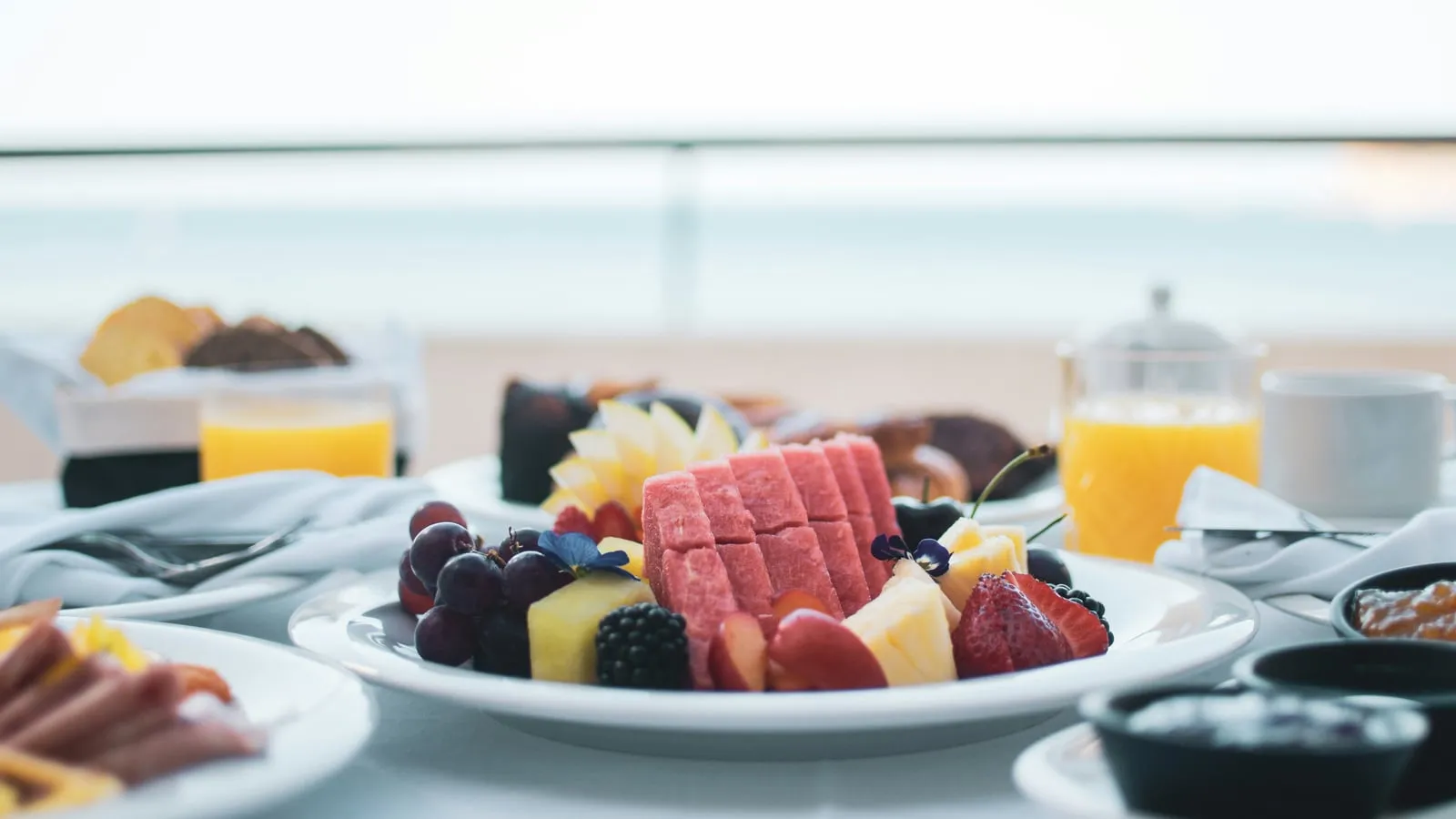 Mesa de café da manhã de hotel com frutas frescas, pães e suco de laranja iluminada por luz natural suave