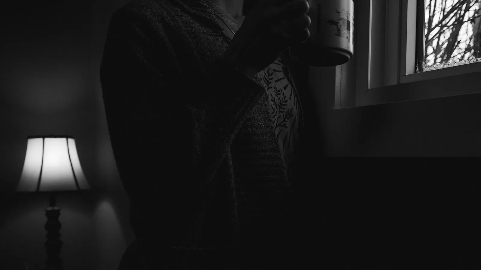 Mulher de costas em pausa contemplativa com xícara de café junto à janela em luz natural suave da manhã