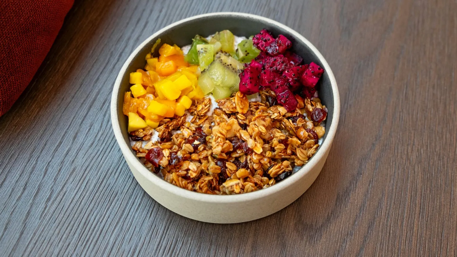Tigela de frutas frescas com kiwi, frutas vermelhas e granola sobre mesa de madeira clara, luz natural suave.